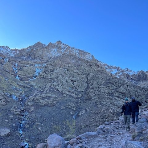 Two people walking towards a rugged mountain area.