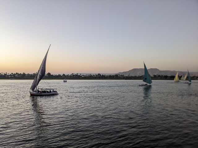 Sailboats on a river during sunset with mountains in the background.