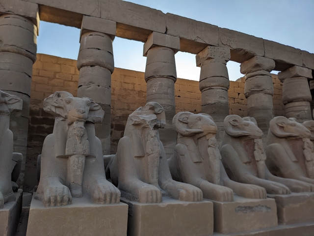 Row of ancient statues with animal heads in front of temple columns.