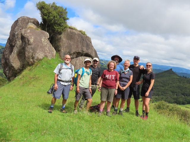       Group of hikers posing on a grassy trail with rocky outcrops.
  