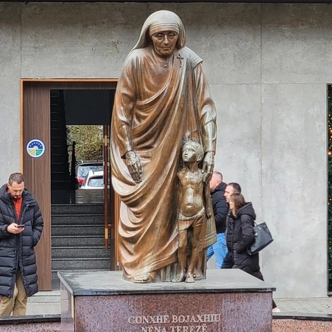      Bronze sculpture of a woman and child near a building.
  