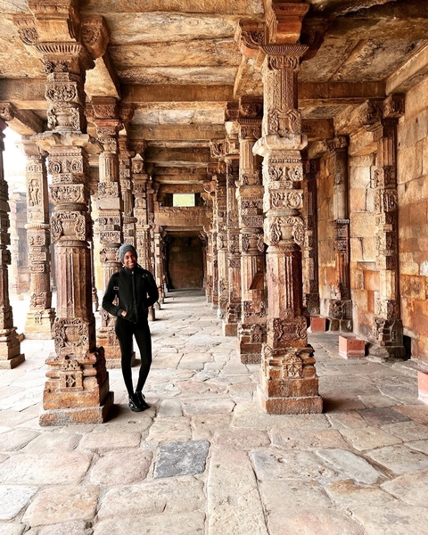 Woman standing in a corridor with carved pillars.