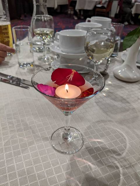       Martini glass with a candle and rose petals on a dinner table.
  
