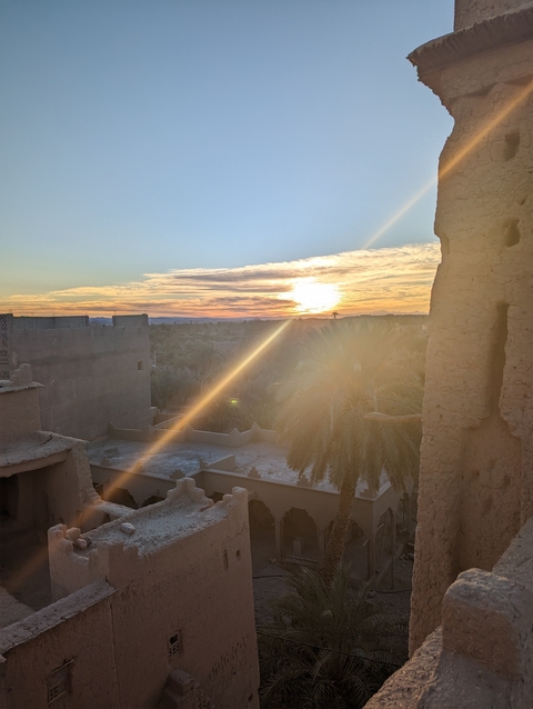       View of a sunset over a town with palm trees and traditional architecture.
  