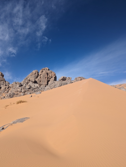       A wide view of a sand dune with rock formations and a blue sky.
  