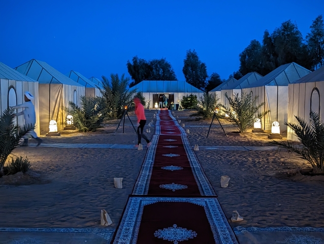       Desert camp with tents and decorative lighting in the evening.
  