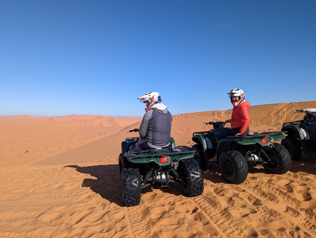       People riding quad bikes on a desert sand dune.
  