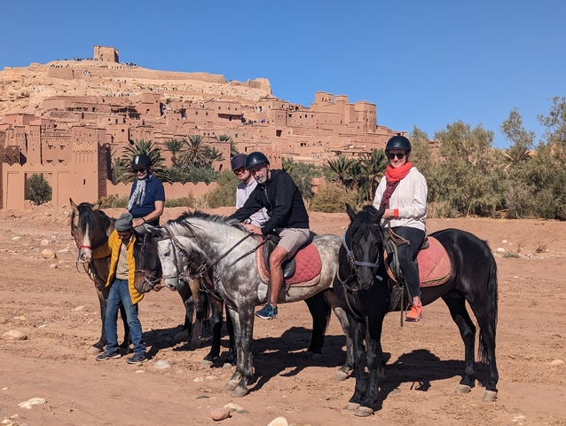       Group of people on horseback with a traditional desert settlement in the background.
  