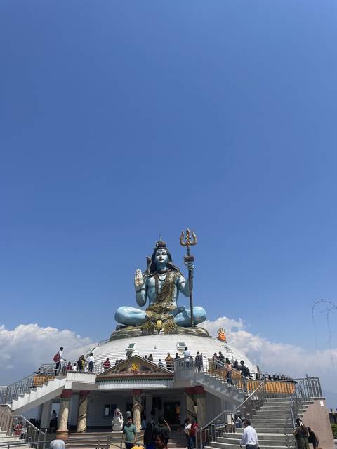 A statue of a blue deity with a trident on a temple roof.