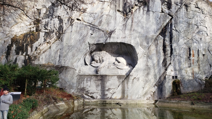 Lion Monument carved into a rock face with people nearby.