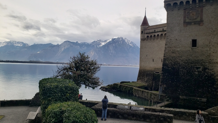 Medieval castle by a lake with mountains in the background.