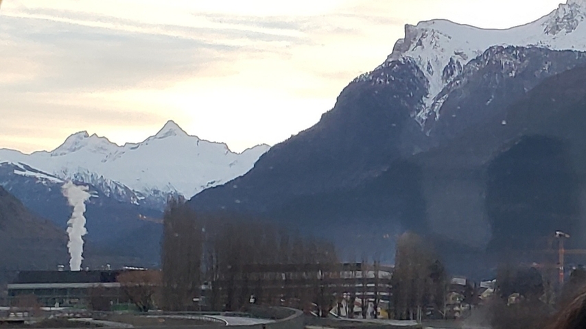 Snow-capped mountains with industrial buildings in the foreground.