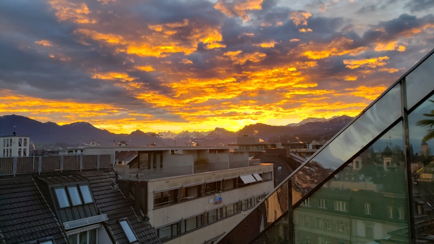 Dramatic sunset over rooftops with mountains in the background.