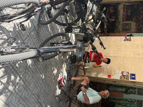       People sitting outside a building with bicycles nearby.
  