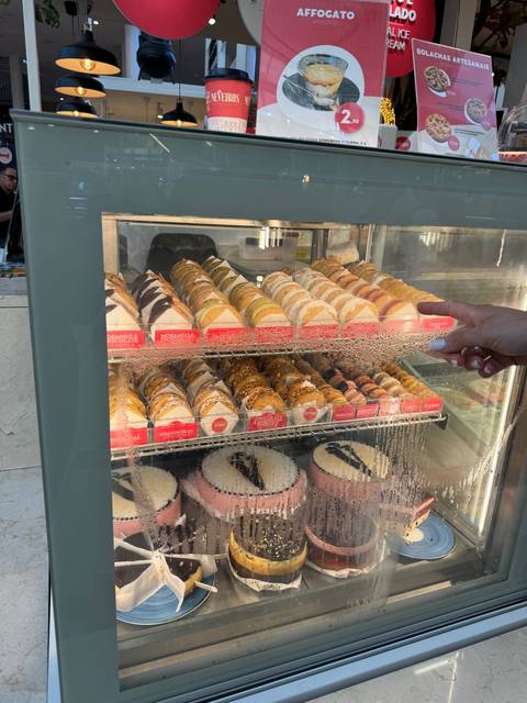       A display of colorful ice cream cones and cakes in a glass refrigerator.
  