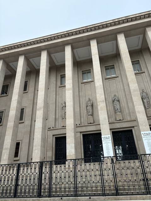      A neoclassical building facade with columns and sculptures.
  