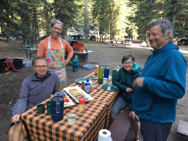       Group of people enjoying a meal at a campsite with trees around.
  