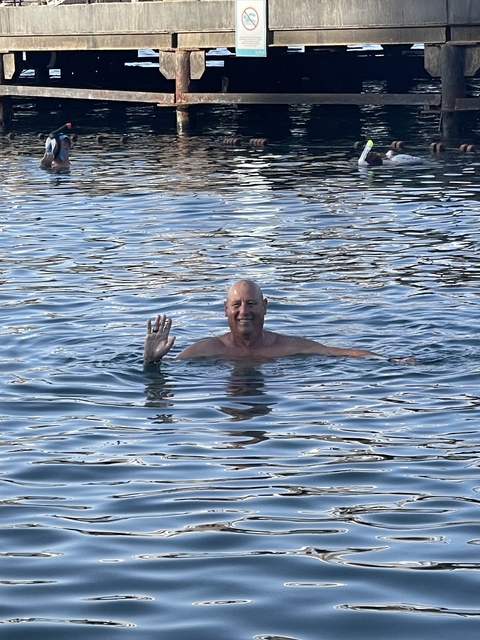 Person swimming in a body of water, waving at the camera.