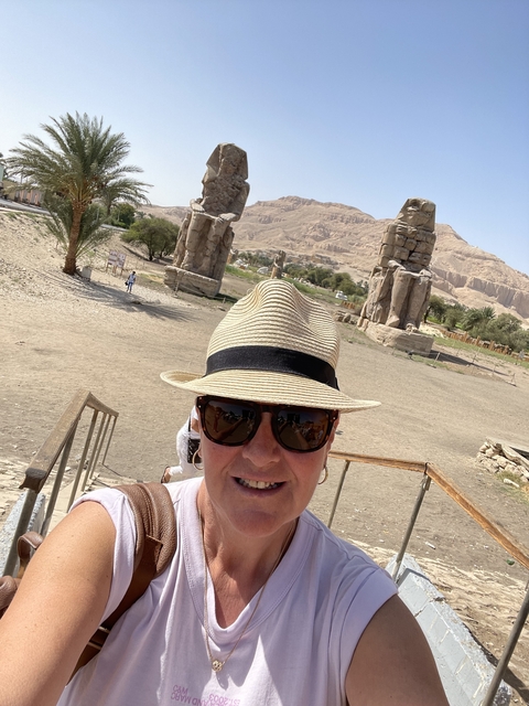 Tourist posing in front of ancient statues with desert landscape.
