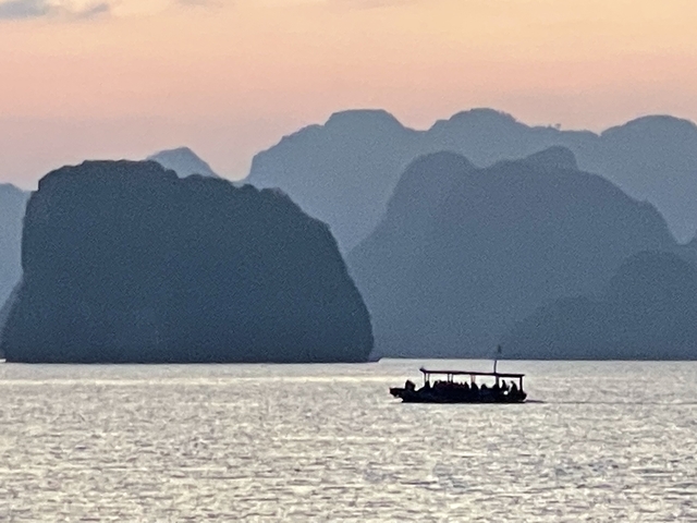       Silhouette of a boat against a backdrop of limestone karsts.
  
