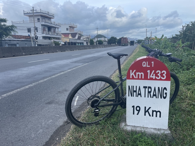       Bicycle parked next to a road marker indicating distance to Nha Trang.
  