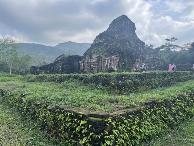       Ancient ruins covered with greenery and people exploring.
  