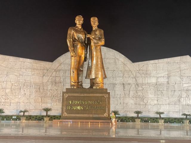       Statue of two figures with illuminated plaques at night.
  