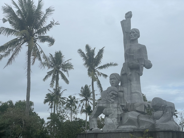       Statue under palm trees on a cloudy day.
  