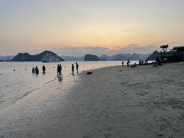       Beach scene at sunset with people and a cruise ship.
  