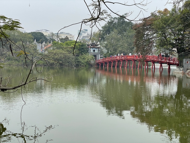       Red bridge over a lake with people walking.
  