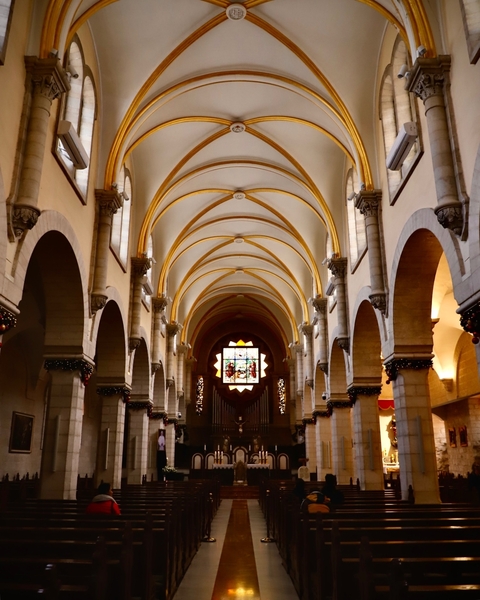       Interior of a church with a stained-glass window and decorated arches.
  