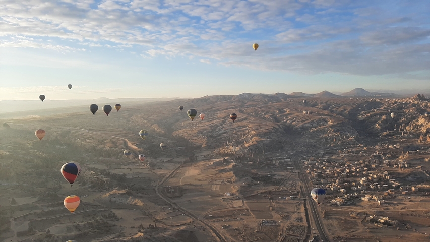       Numerous colorful hot air balloons in flight over a rocky landscape.
  