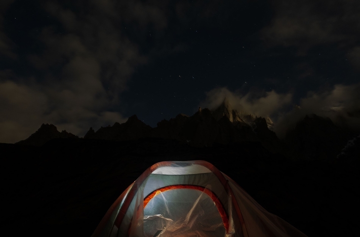 Tent illuminated at night with starry sky above.