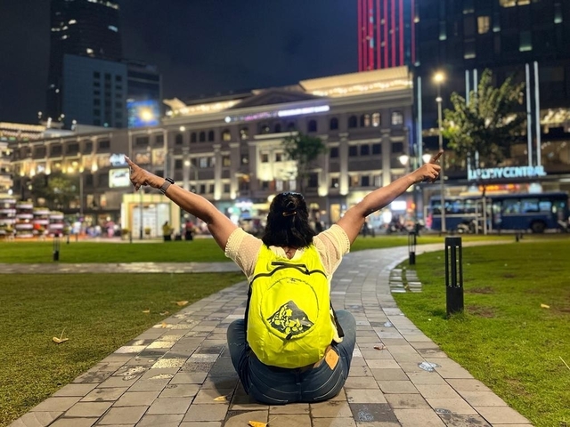       Person posing with arms raised in a vibrant urban setting at night.
  