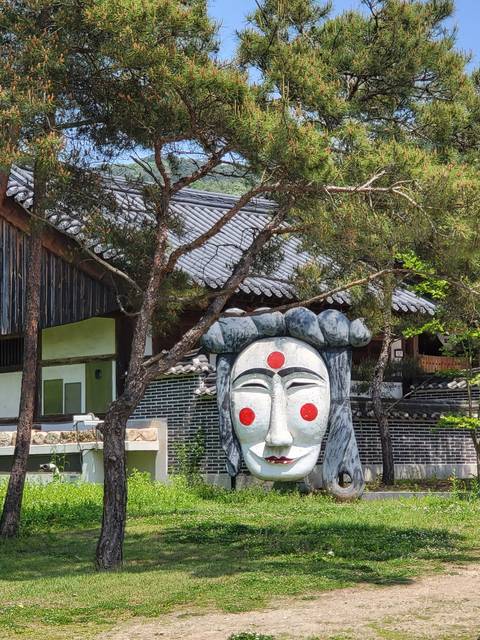 Large mask sculpture near trees.