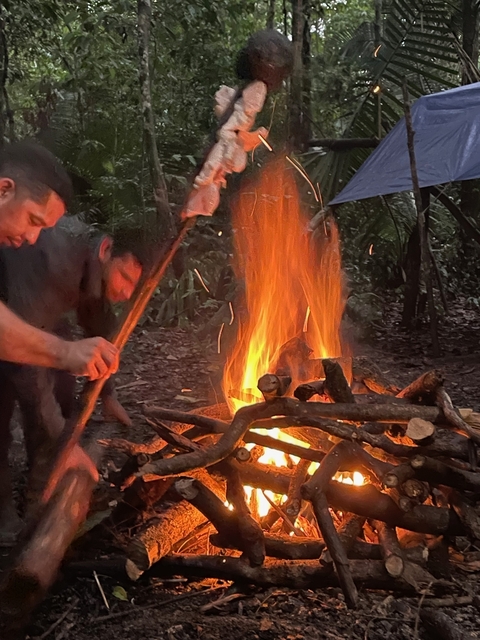       A campfire with people around in a forest setting.
  