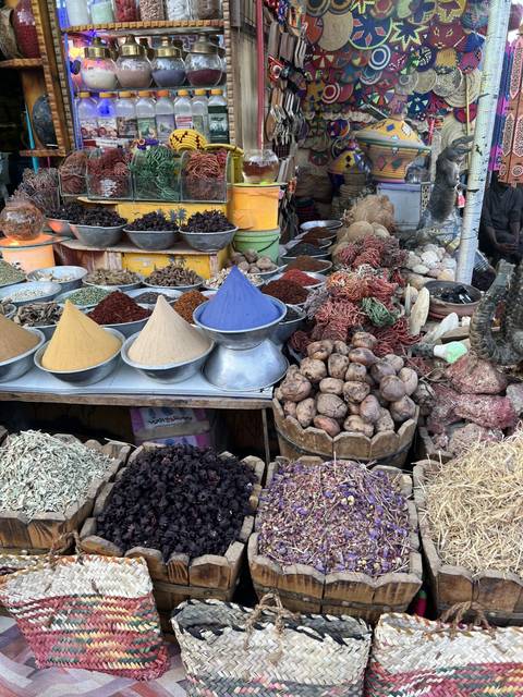 Market stall with various spices and grains in baskets and containers.