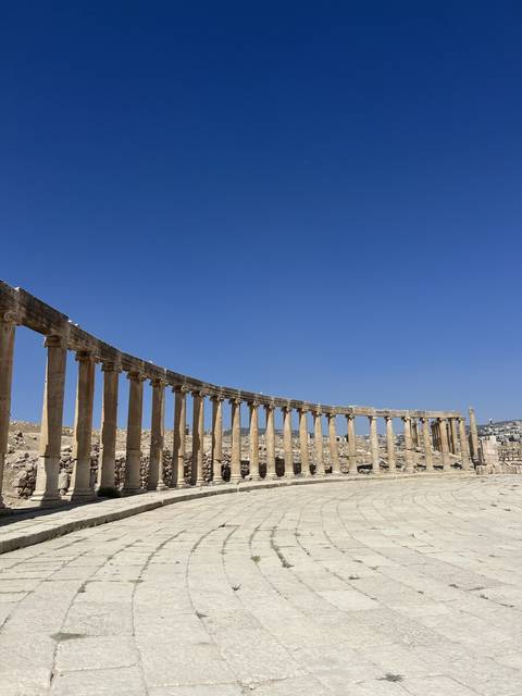       Curved ancient stone columns under a clear blue sky.
  