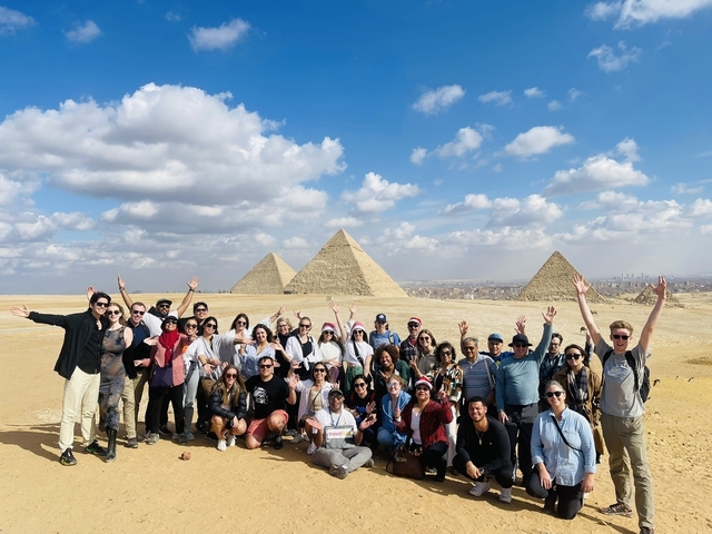       Large group of people raising their hands near the pyramids.
  