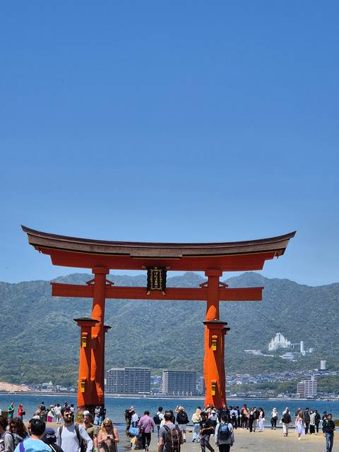       Crowded area with large red torii gate and mountains.
  