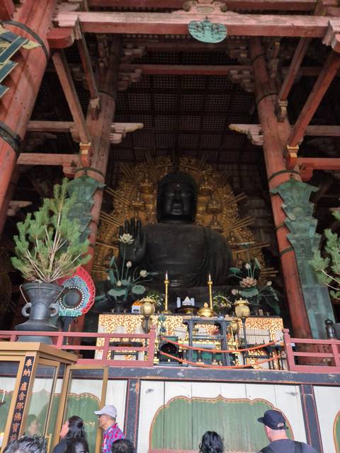       Large indoor Buddha statue with visitors around.
  