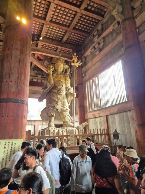       Statue inside a temple with visitors around.
  