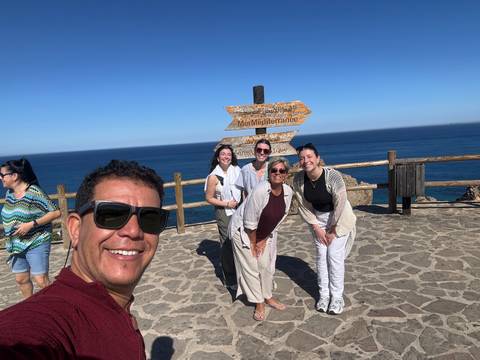 Group of people posing next to a directional sign near the ocean.