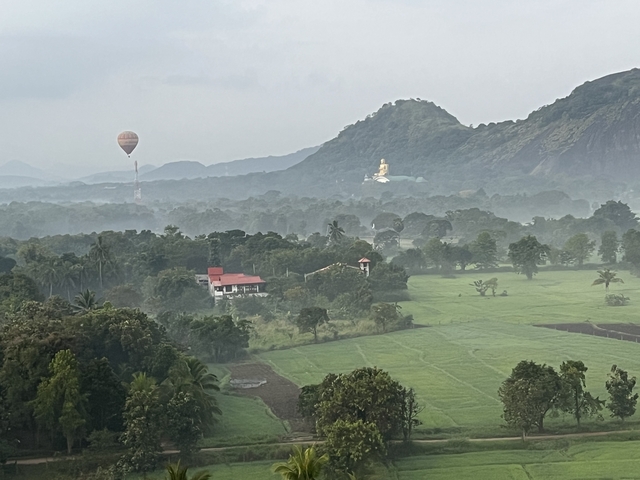 Foggy landscape with a hot air balloon and a distant statue.