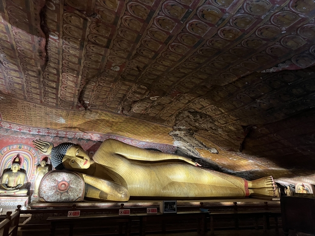 Reclining Buddha statue inside a temple with intricate ceiling artwork.
