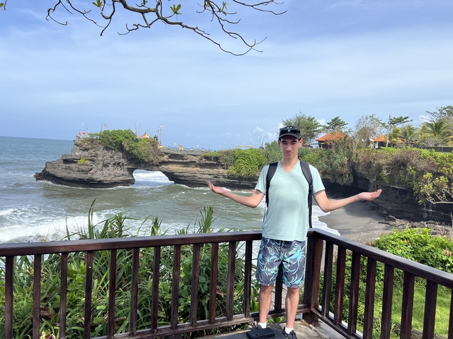       Person standing on a balcony with a coastal view and rock formations.
  