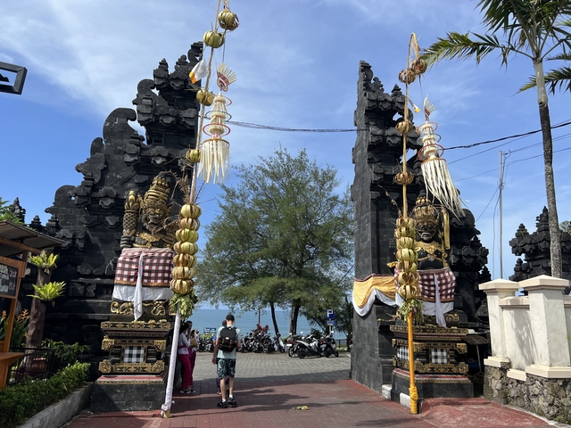       Traditional entrance gate with statues and distant view of the sea.
  