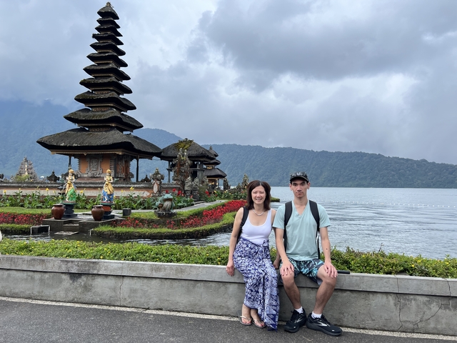       Two people sitting with a traditional temple and water in the background.
  