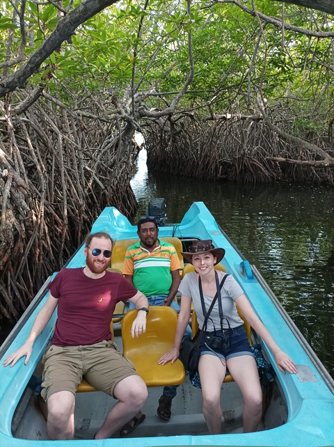 Group on a boat in a narrow waterway surrounded by mangroves.