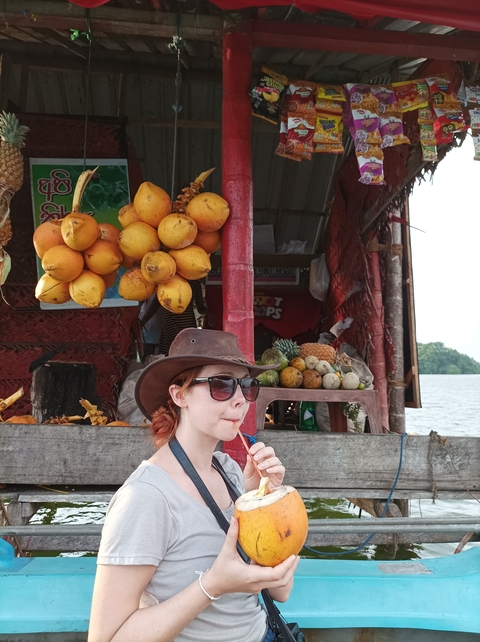 Person sitting by a fruit stall enjoying a drink.